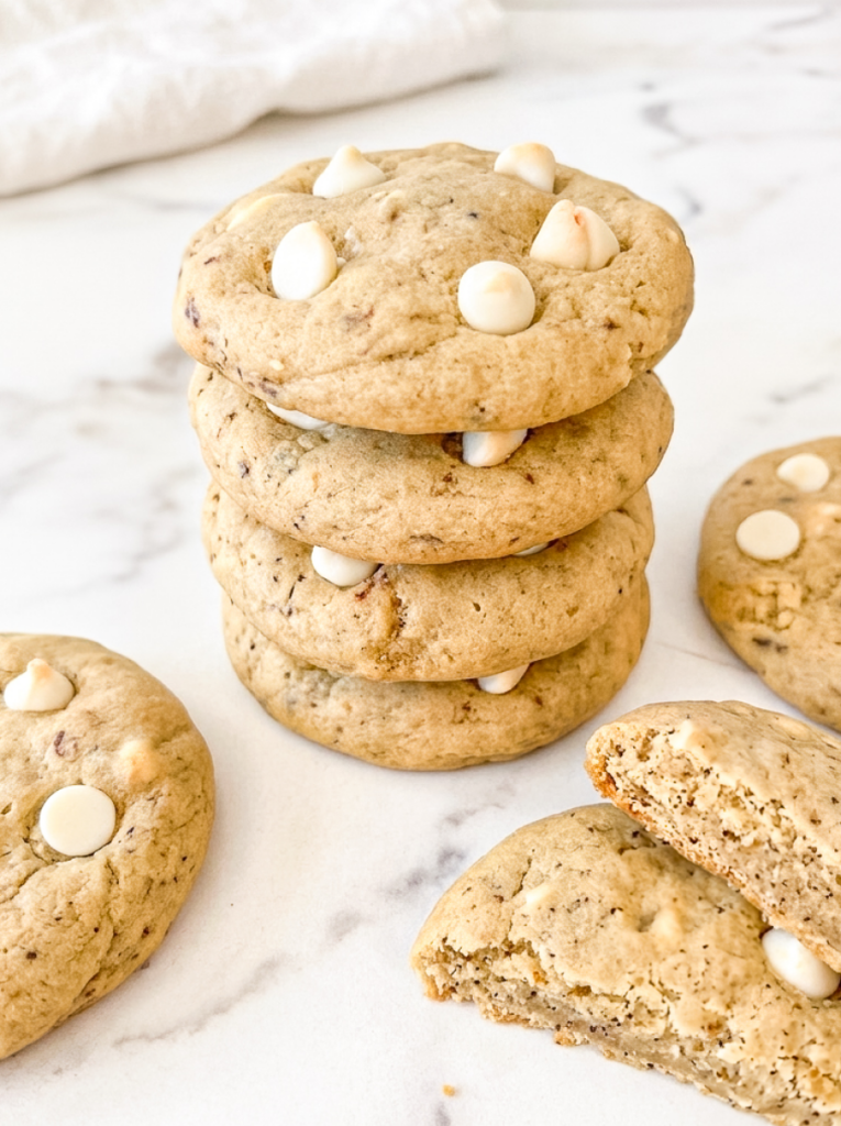 Stack of four coffee-speckled cookies studded with white chocolate chips on a white marble surface, with additional cookies arranged around the stack and one cookie broken in half to show the soft, tender interior.