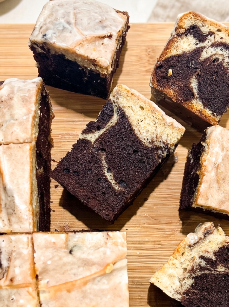 Square slices of marbled cake with swirled chocolate and cinnamon layers topped with cinnamon sugar glaze, arranged on a wooden cutting board with several pieces standing upright to show the interior marbling pattern.