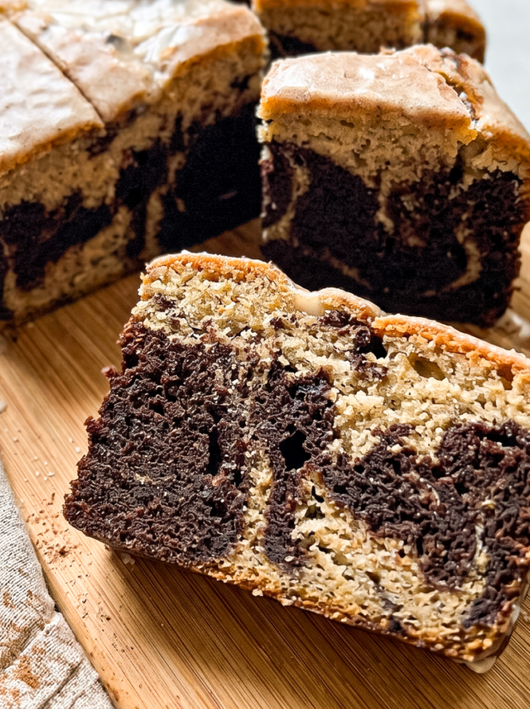 Sliced marble cake on a wooden cutting board showing swirled cinnamon and chocolate layers with a crunchy cereal-coated top. The close-up angle reveals the moist crumb texture with distinct dark and light swirls throughout each slice.