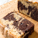 Sliced marble cake with cinnamon sugar swirls of dark chocolate and tan cake, topped with cinnamon glaze, displayed on a bamboo cutting board with one slice in foreground