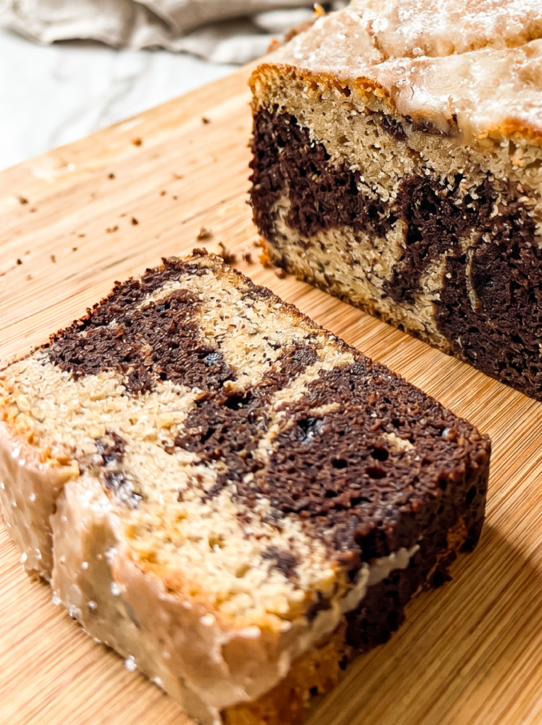 Sliced marble cake with cinnamon sugar swirls of dark chocolate and tan cake, topped with cinnamon glaze, displayed on a bamboo cutting board with one slice in foreground