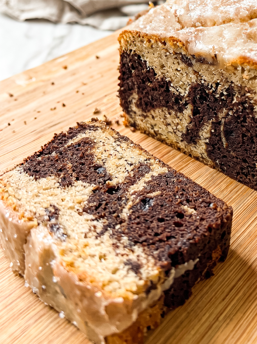 Sliced marble cake with cinnamon sugar swirls of dark chocolate and tan cake, topped with cinnamon glaze, displayed on a bamboo cutting board with one slice in foreground
