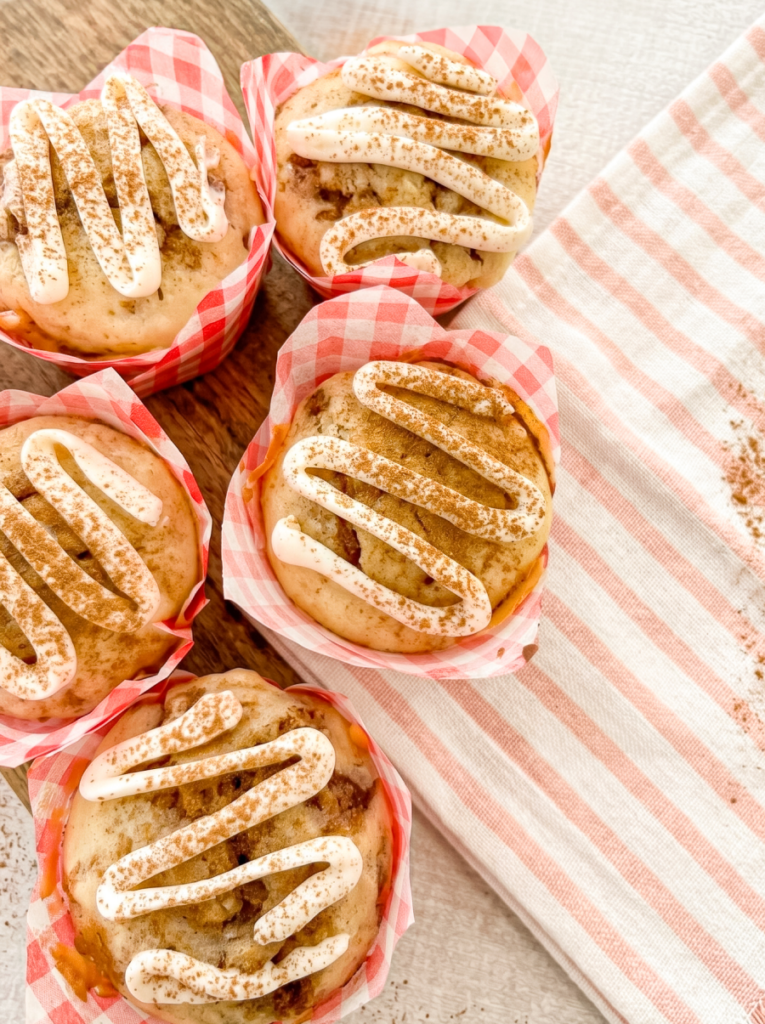 Four cinnamon roll muffins in red gingham liners with white icing and cinnamon sprinkles.