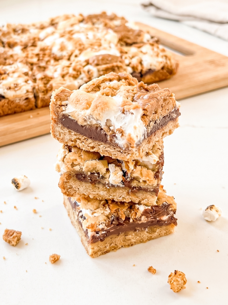 Three biscoff s'mores bars are stacked on a white surface, showing gooey chocolate,
