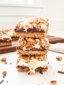 A stack of three biscoff s'mores bars with gooey melted chocolate and toasted marshmallows, crumbs scattered on a white counter.