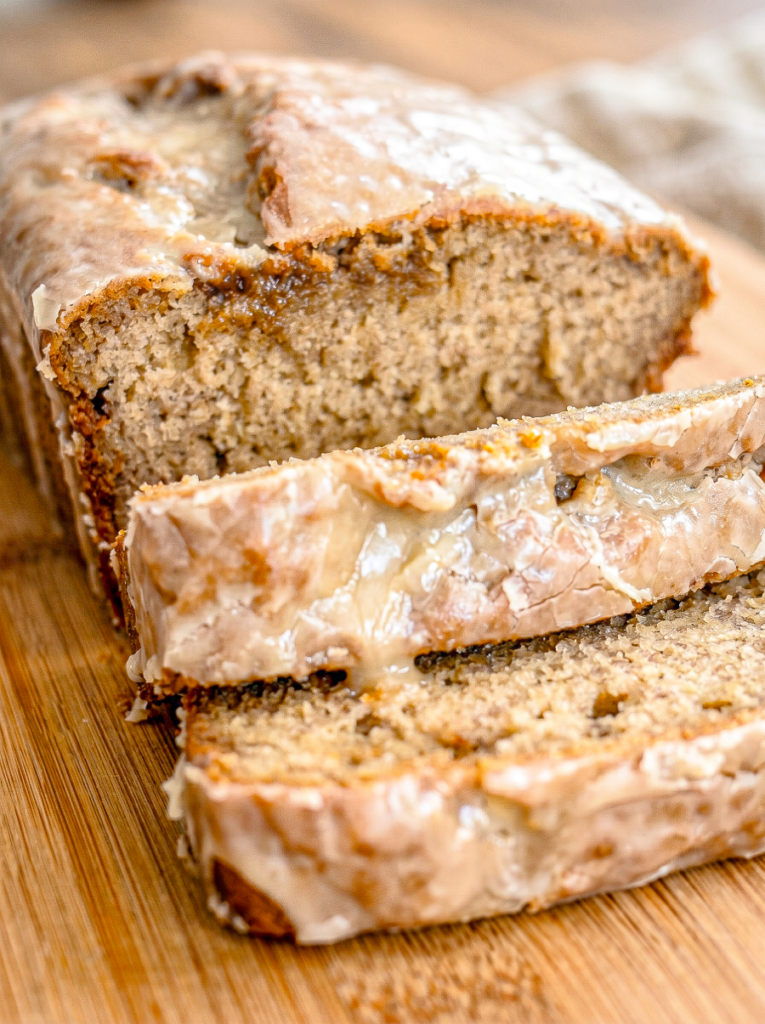 Sliced banana bread loaf with coffee-colored crumb and glossy white glaze drizzled over top, displayed on a wooden cutting board with two thick slices cut and laid in front.