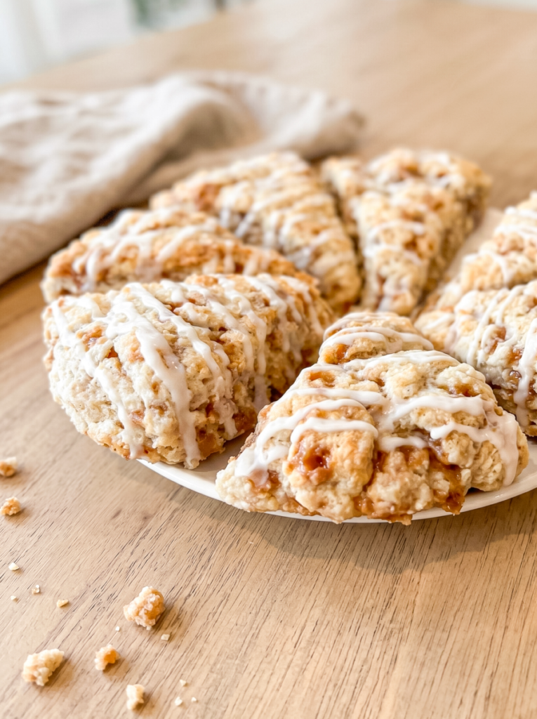 A white plate holds triangular cinnamon toffee scones drizzled with white icing on a wooden table.