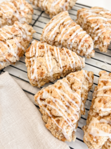 Several triangular cinnamon toffee scones with white icing drizzle are cooling on a black wire rack, with a linen napkin nearby.