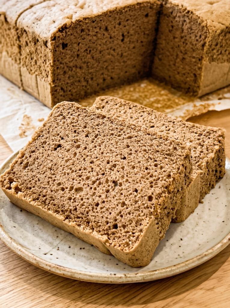 Two slices of porous brown hojicha castella cake are on a speckled plate, with the remaining loaf on parchment paper in the background.