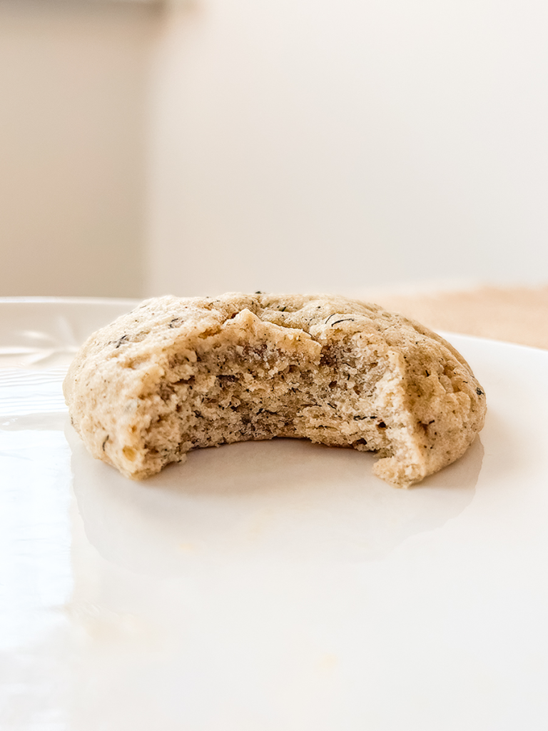 A soft, light brown banana cookie with a bite taken out, revealing its moist texture, rests on a white plate.