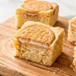 Golden Oreo blondies on a wooden board, with a visible cream-filled cookie half embedded in each square.