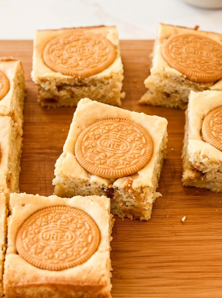 Golden Oreo blondies on a wooden board, with a visible cream-filled cookie half embedded in each square.
