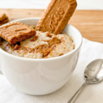 A white mug holds a fluffy Biscoff mug cake topped with a whole Biscoff cookie, a broken piece, and melted Biscoff spread.
