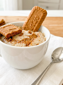A white mug holds a fluffy Biscoff mug cake topped with a whole Biscoff cookie, a broken piece, and melted Biscoff spread.