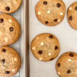 Freshly baked golden cookies with dark and white chocolate chips cooling on a wire rack and a parchment-lined baking sheet.