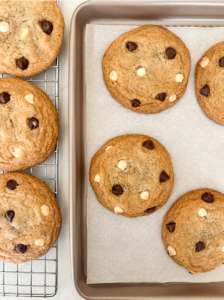 Freshly baked golden cookies with dark and white chocolate chips cooling on a wire rack and a parchment-lined baking sheet.