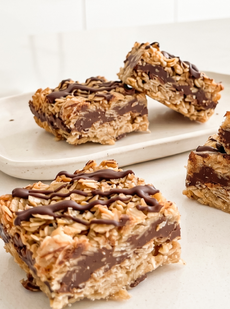 Three no-bake chunky chocolate oat bars with a thick chocolate layer and drizzle are on a white plate.
