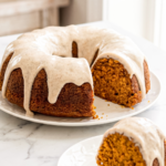 A pumpkin maple bundt cake with a slice cut out, both pieces glazed, resting on white plates on a marble countertop.