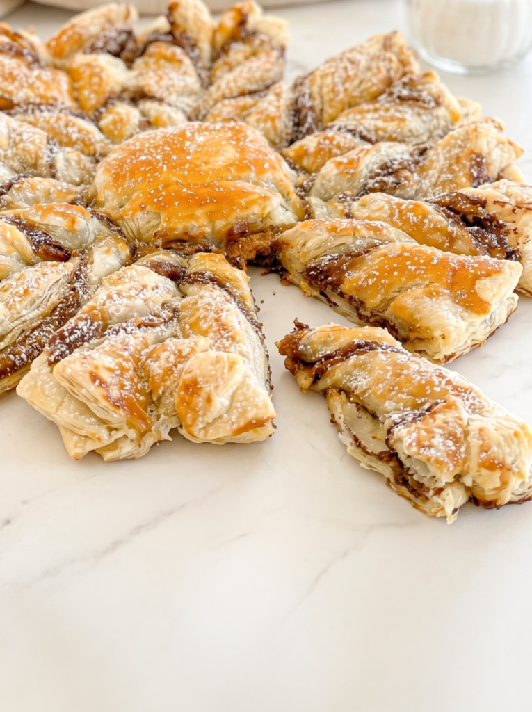 My baked puff pastry snowflake is filled with Nutella and Biscoff, dusted with powdered sugar, with one piece pulled away.