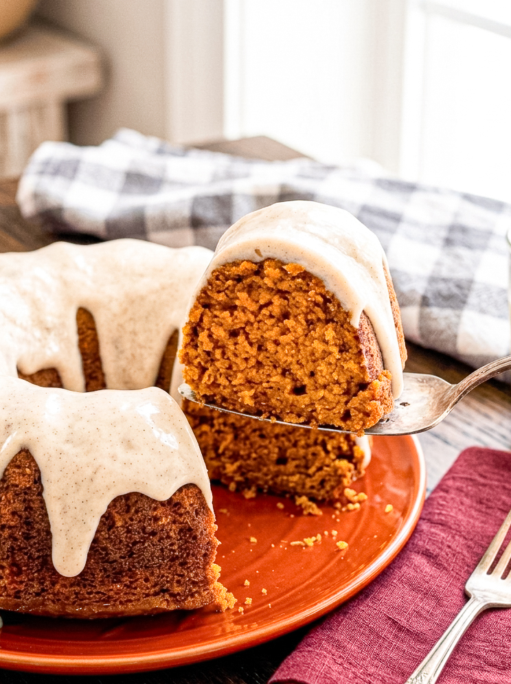pumpkin maple bundt cake slice lifted from a red plate and a burgundy napkin on the table.