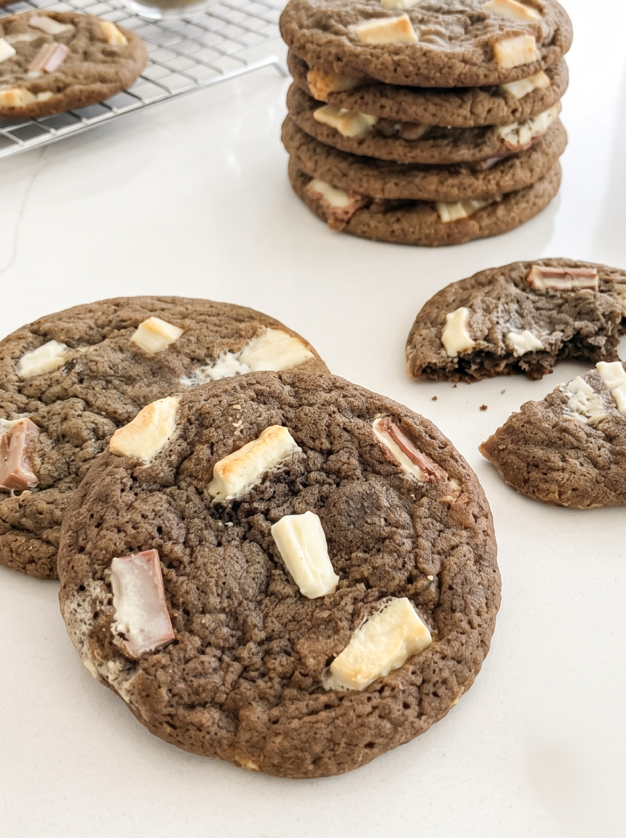 Hojicha latte cookies with white and light brown chocolate chunks are arranged on a white surface, with a stack and a broken cookie visible.