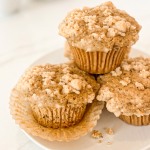 Three Earl Grey muffins with a crumble topping on a white plate, with one muffin's paper liner pulled back.