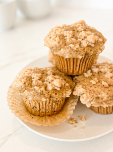 Three Earl Grey muffins with a crumble topping on a white plate, with one muffin's paper liner pulled back.