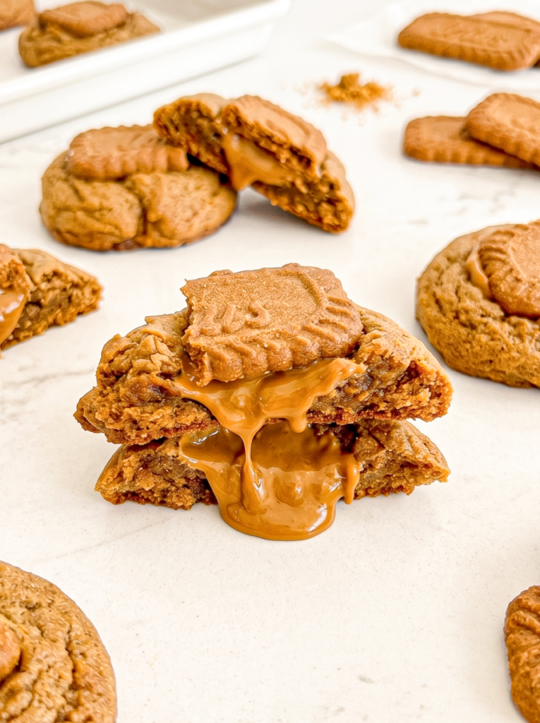A gingerbread cookie is broken in half, showing a gooey Biscoff spread centre, with a Biscoff biscuit piece on top.