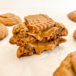 Gingerbread cookie split open, revealing Biscoff spread oozing from its centre, topped with a Biscoff cookie.