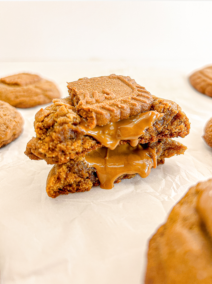 Gingerbread cookie split open, revealing Biscoff spread oozing from its centre, topped with a Biscoff cookie.