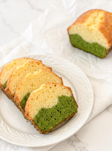 Four slices of a matcha latte pound cake with green bottom and light yellow top layers are arranged on a white plate, with the rest of the loaf in the background.