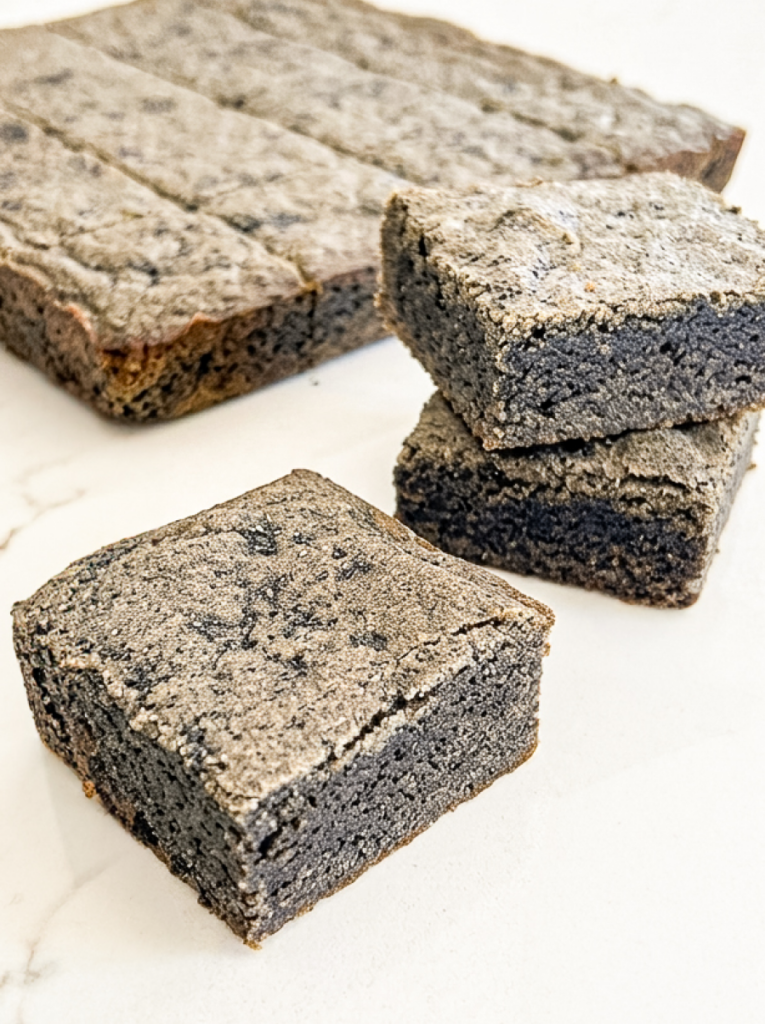 Black sesame blondies with a dark grey colour and a light grey, textured top are arranged on a white marble surface.