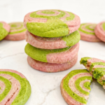 A stack of four strawberry and matcha pinwheel cookies with a broken cookie showing the swirl on a marble surface.