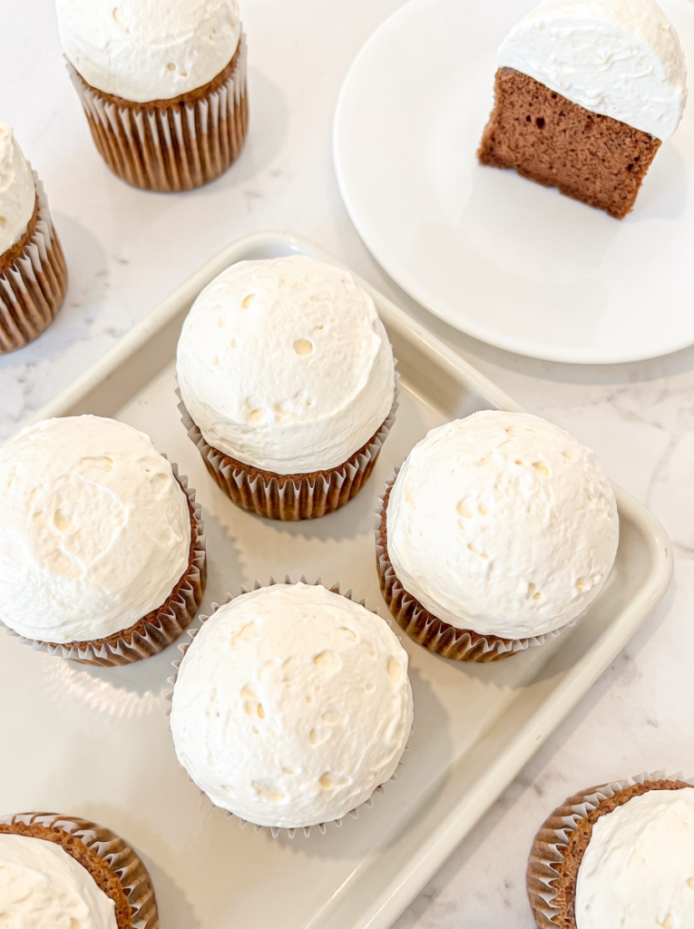 Hokkaido mocha chiffon cupcakes topped with white frosting are on a tray, with one cut piece on a plate.