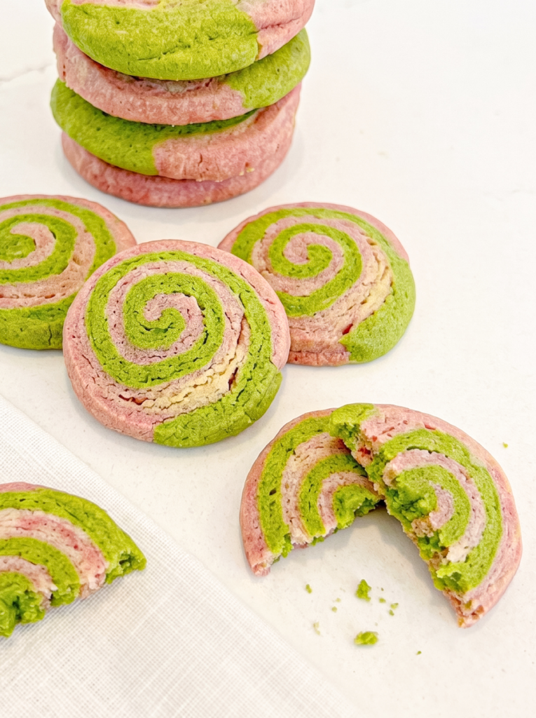 St= and green spiral cookies are stacked, with others scattered on a white surface, and one broken in half to show the swirled interior.