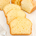 Slices of pound cake with a golden crust are arranged on white parchment paper, with a fork in the foreground.