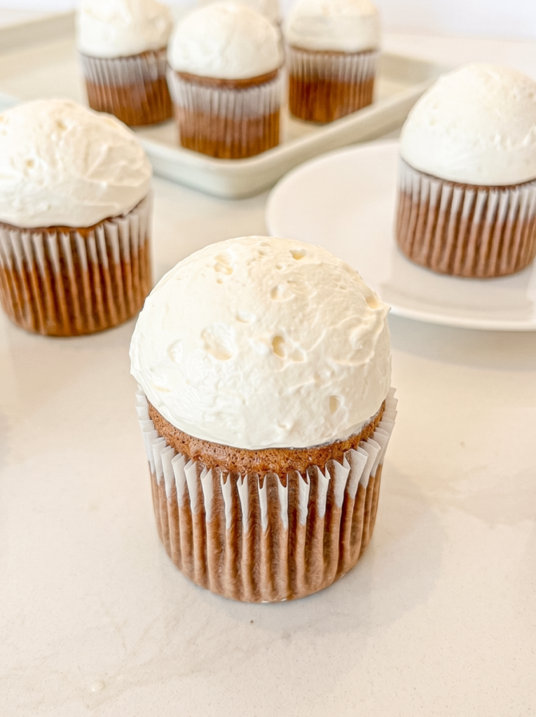A Hokkaido mocha chiffon cupcake with a tall dome of white frosting sits in the foreground, with several other frosted cupcakes behind it.