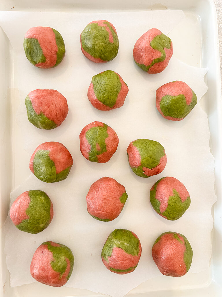 Arranged fifteen balls of pink and green marbled cookie dough on parchment paper on a white baking sheet.