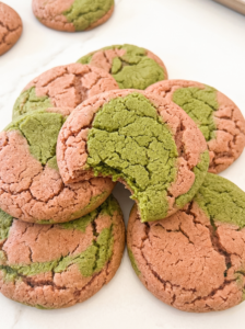 A pile of pink and green marbled cookies, one with a bite taken out, showing its textured surface.