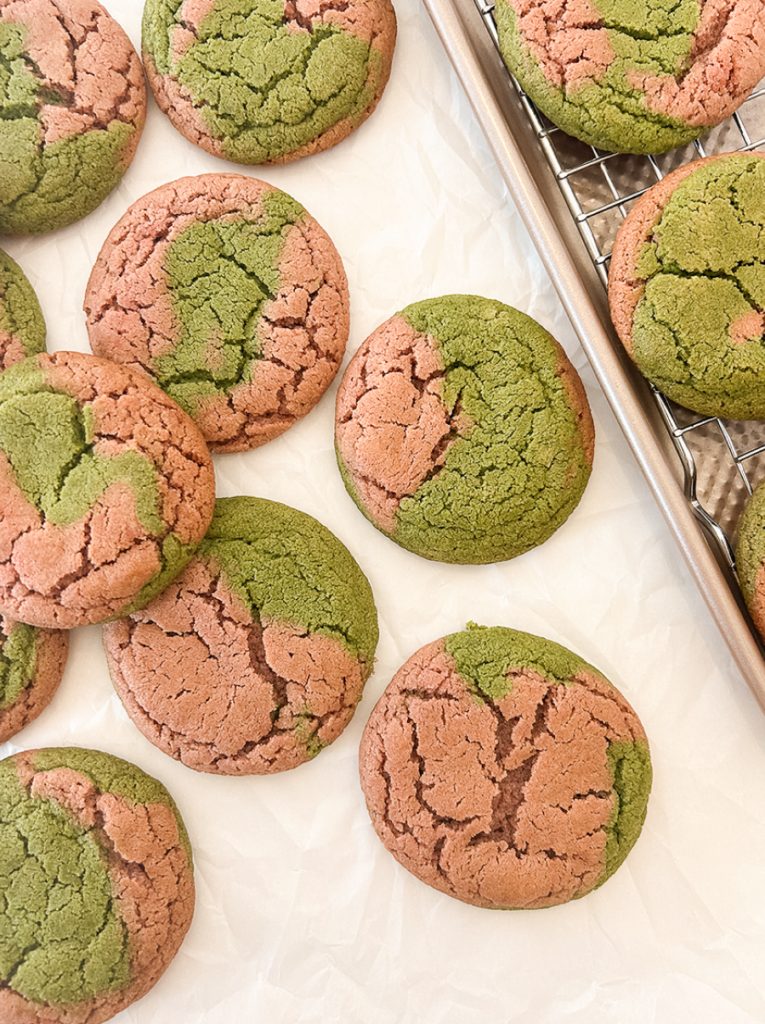 Several round strawberry matcha cookies with green and pink marbled colours on white parchment and a wire rack.