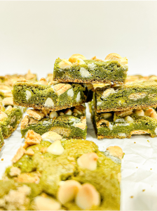 I hold up a square matcha bar with white chocolate chips, melted marshmallow, and graham cracker pieces, with more bars in the background.