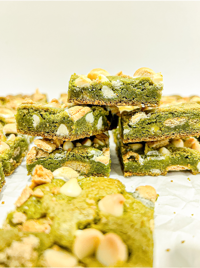 I hold up a square matcha bar with white chocolate chips, melted marshmallow, and graham cracker pieces, with more bars in the background.