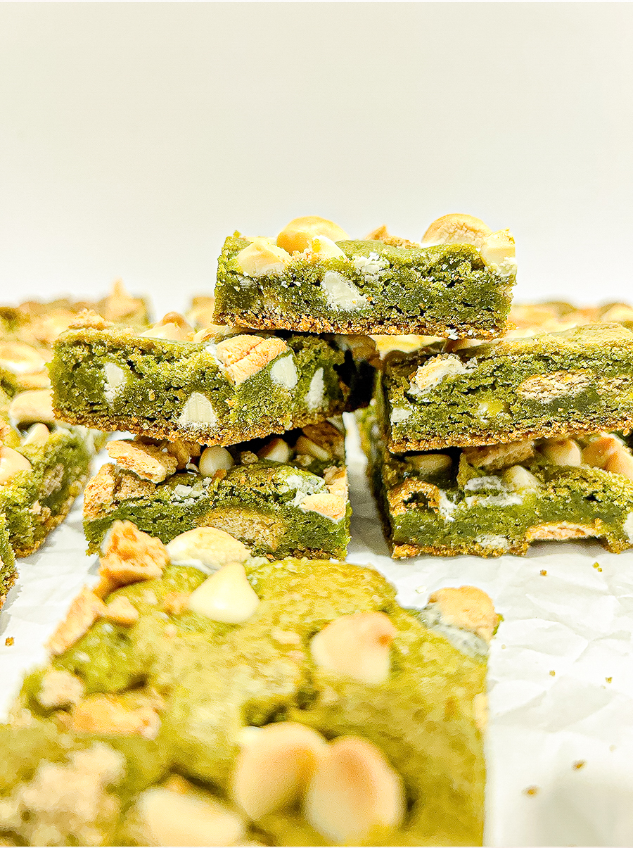 I hold up a square matcha bar with white chocolate chips, melted marshmallow, and graham cracker pieces, with more bars in the background.