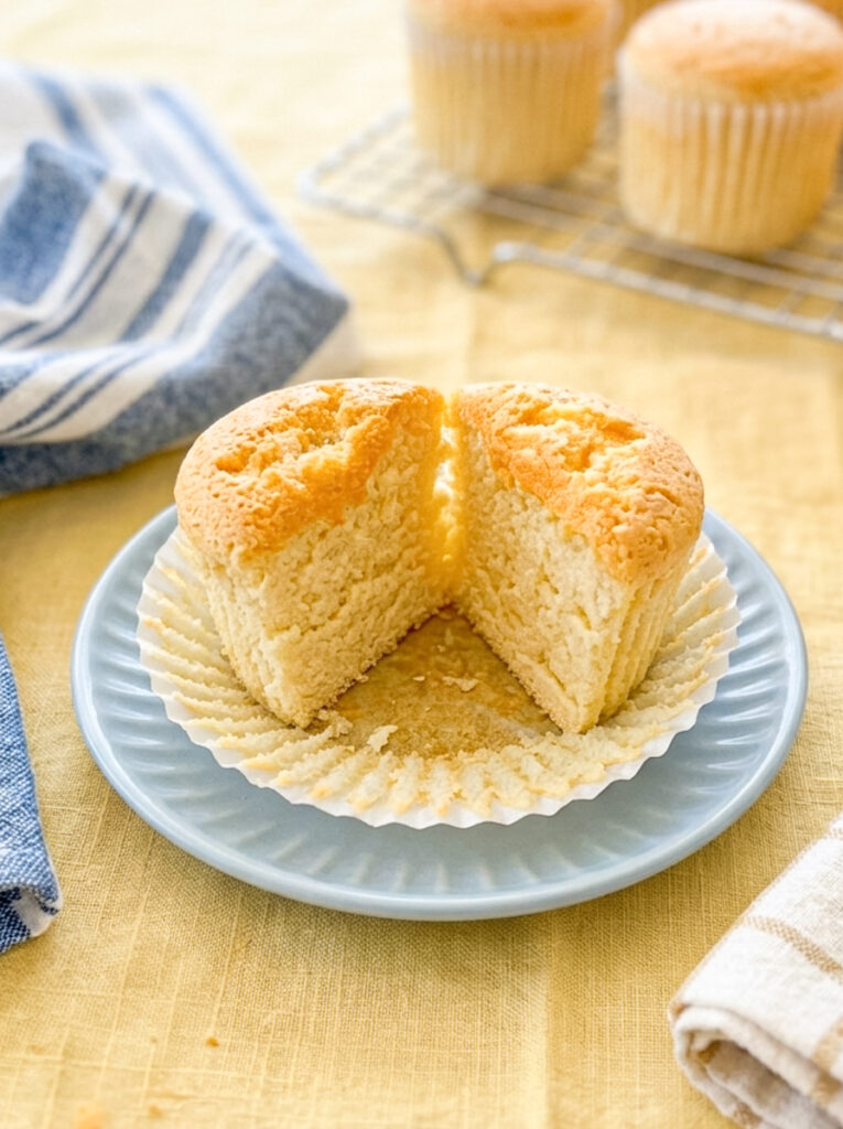 A honey castella muffin cut in half to show the soft crumb at the centre, resting on a blue plate over a yellow tablecloth.