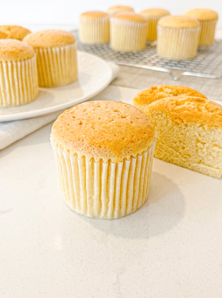 A honey castella muffin in a paper liner is in the foreground, with sliced castella cake and more muffins behind it.