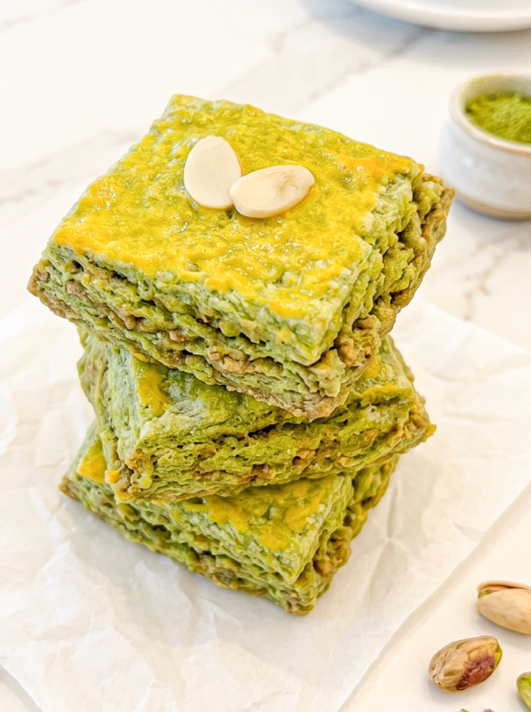 A stack of three square green matcha scones with golden tops, garnished with two almond slivers, rests on white parchment paper.
