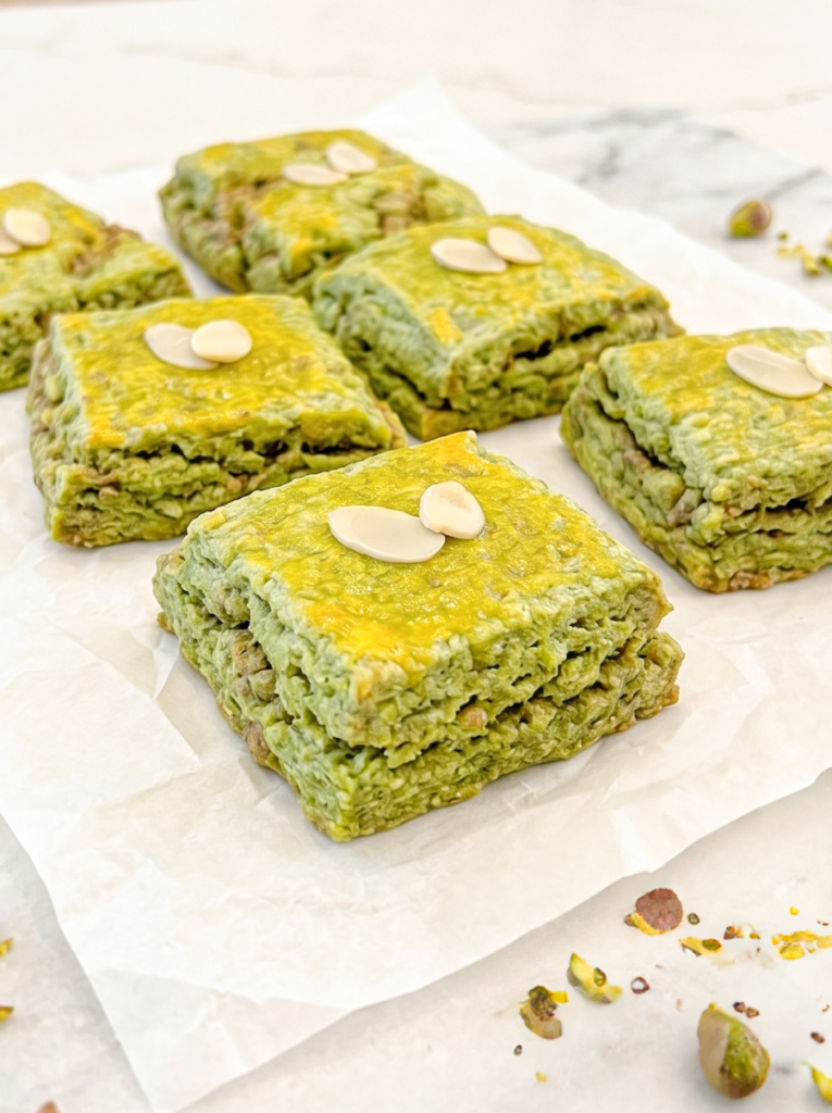 Square pistachio matcha scones have flaky layers and almond slivers on top, resting on parchment paper.