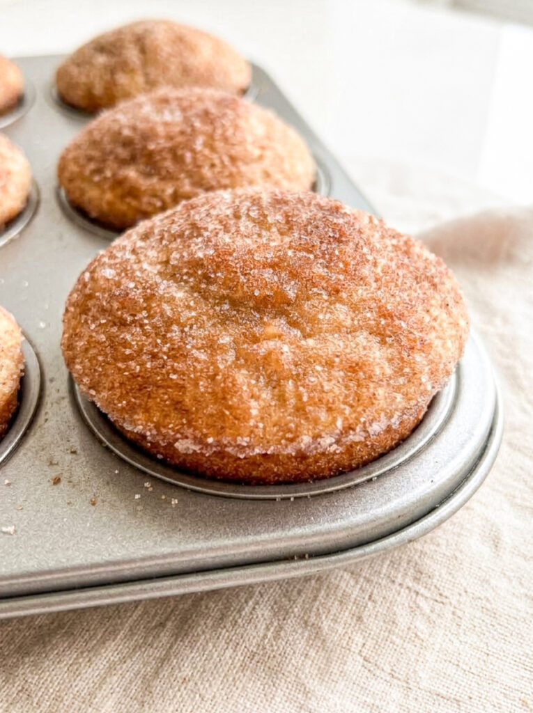Golden-brown cinnamon sugar donut muffins coated in granulated sugar inside a metal baking tin.