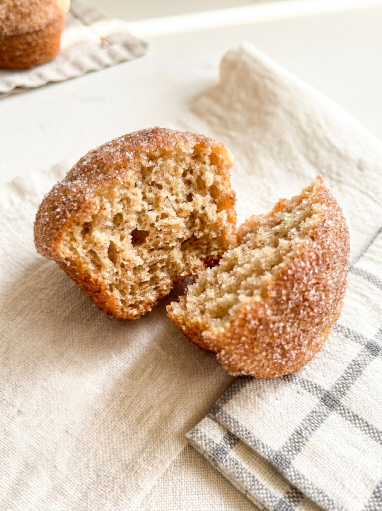 A cinnamon sugar donut muffin split in half on a linen napkin, showing the soft interior crumb.