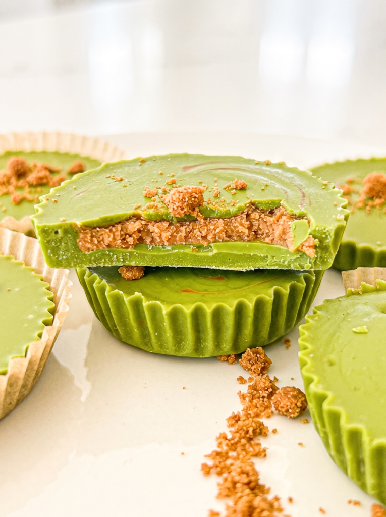 Green matcha cups filled with a biscoff crumb centre are arranged on a white surface, with one cup cut in half.